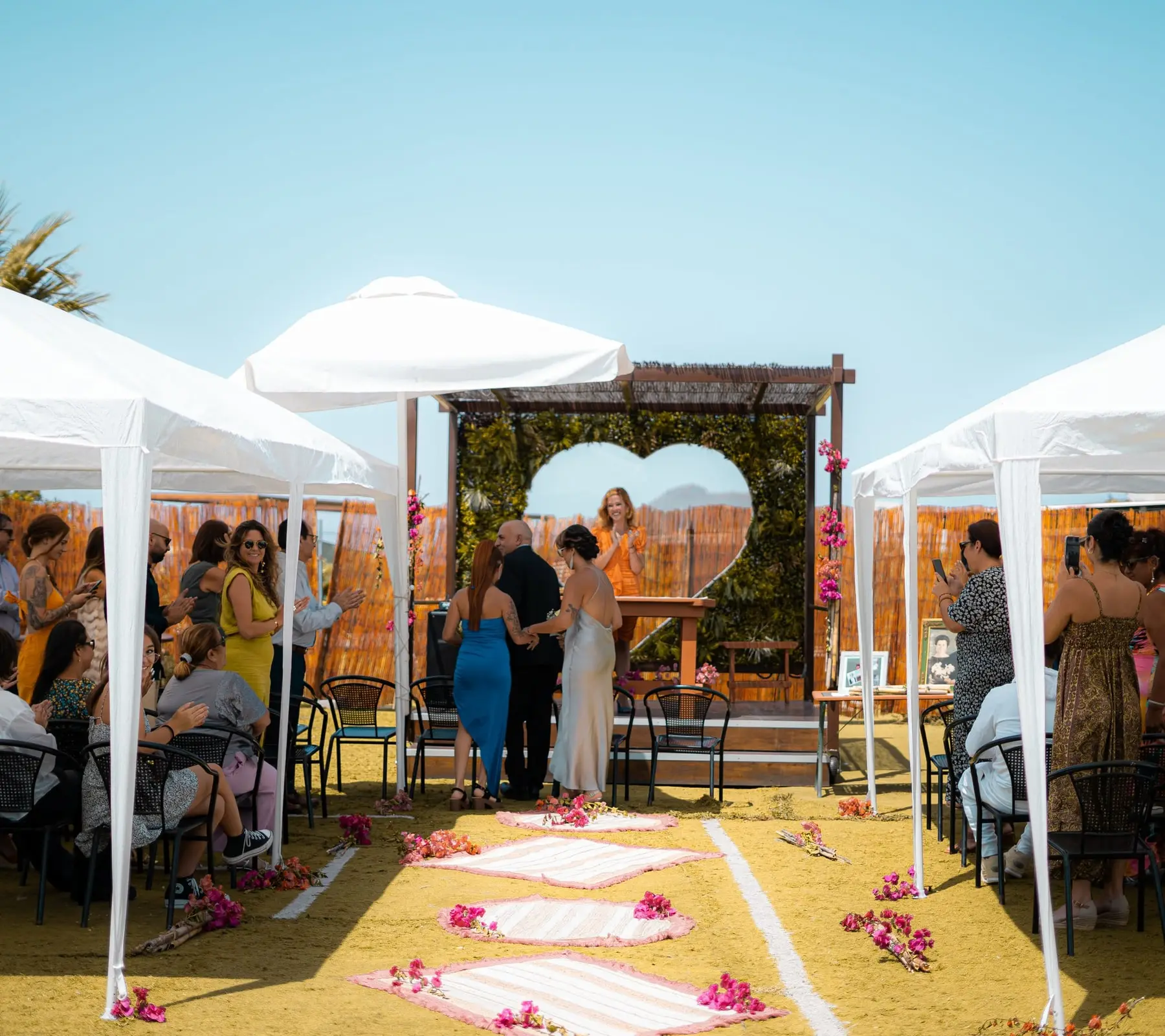 Ceremonia en el corazón: carpas blancas, invitados sentados y un pasillo de alfombras con buganvilla