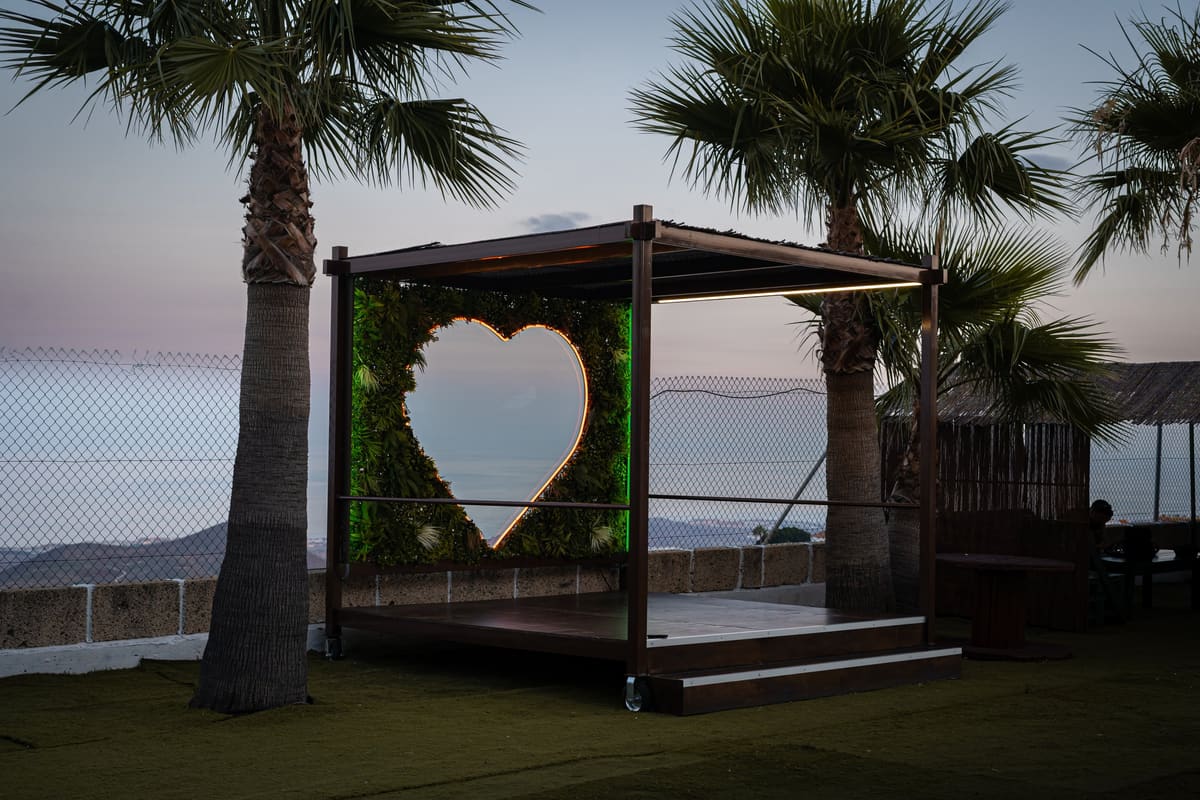 La terraza de Finca El Tablero al anochecer: la tarima del corazón, con su luz encendida, entre palmeras y con el mar al fondo